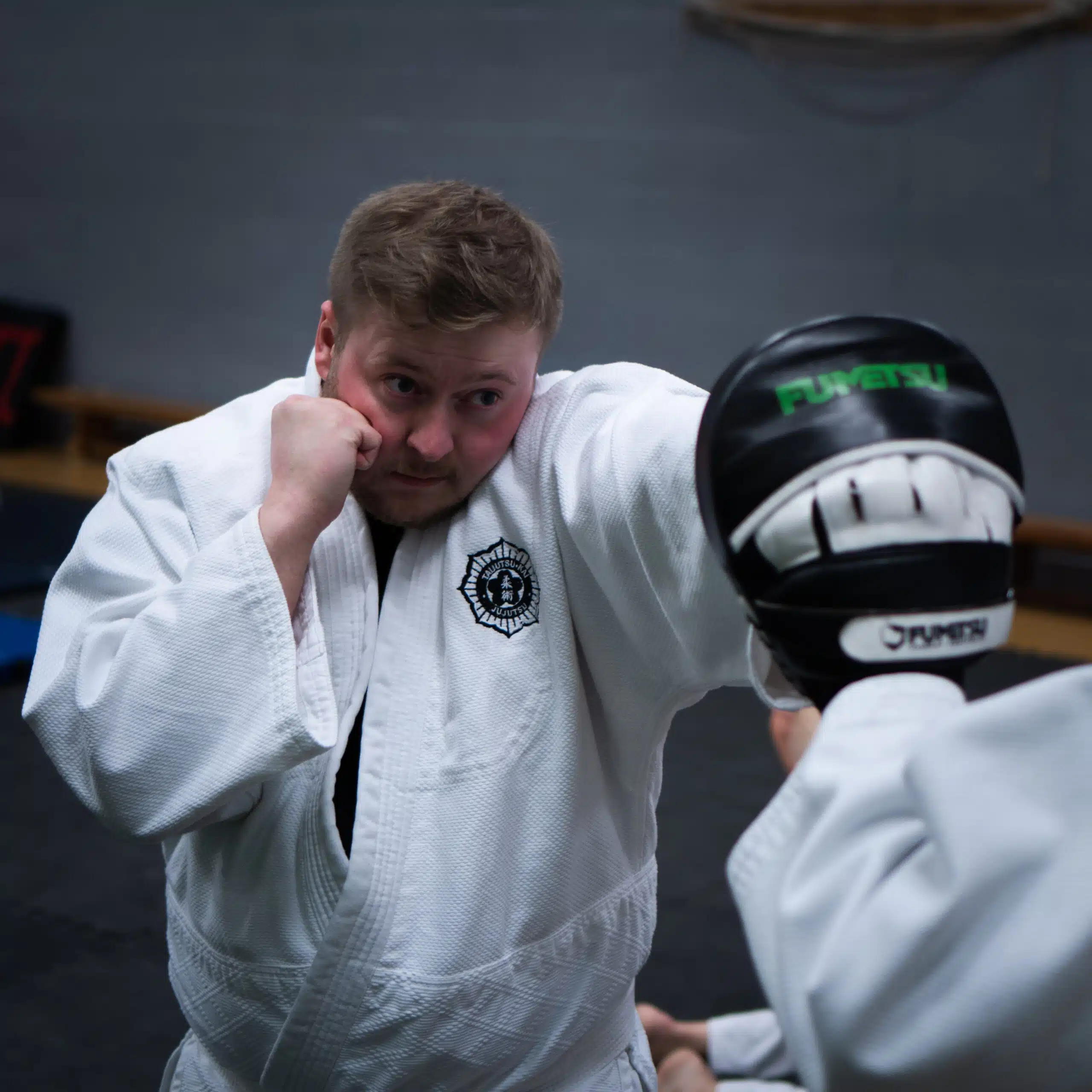 Jujutsu student in a gi throwing a punch at a focus mitt during striking practice