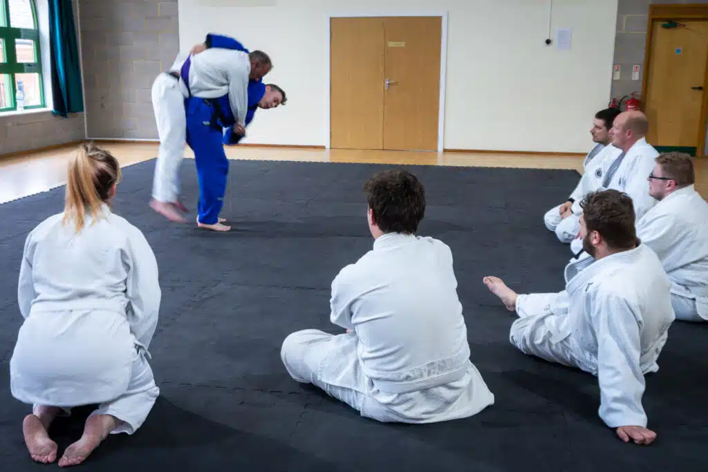Students kneeling at the edge of the mat watching a technique being demonstrated