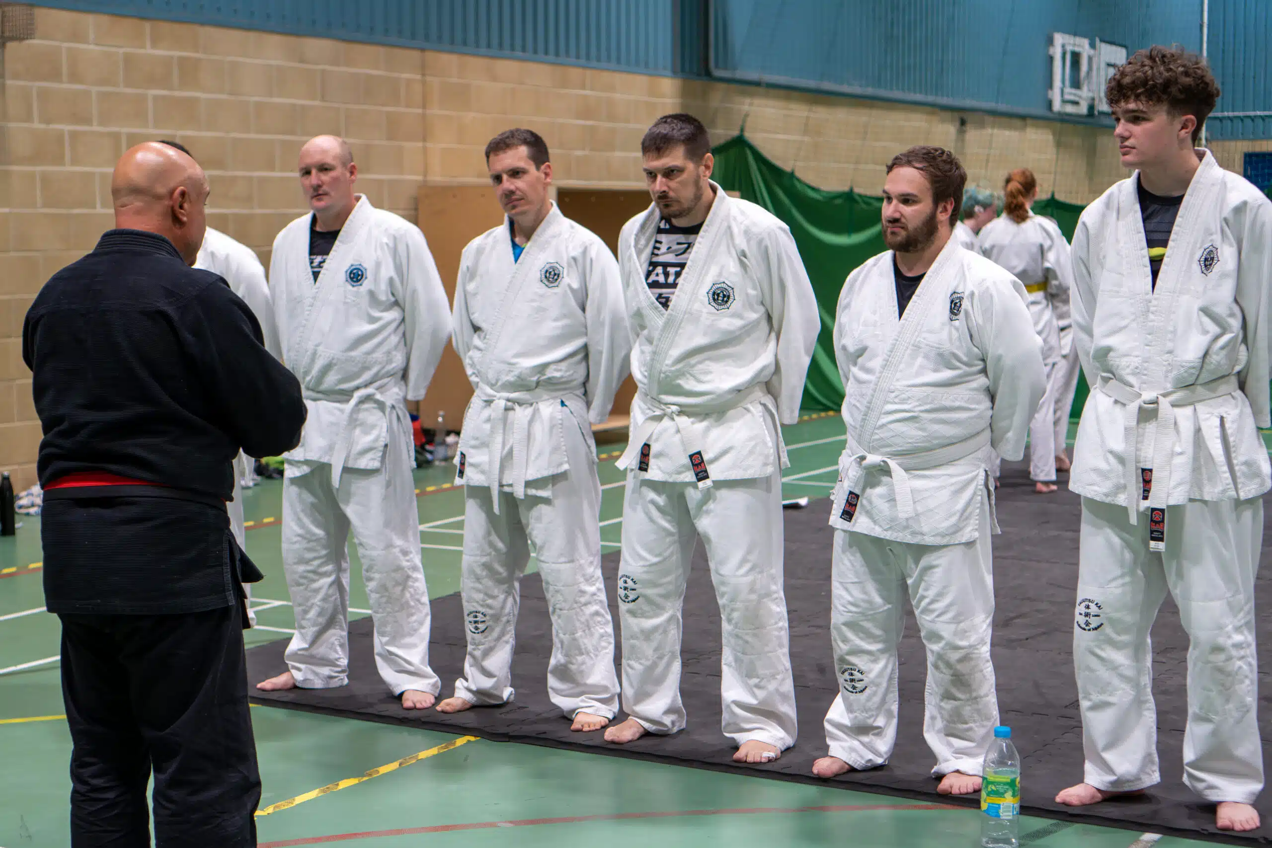 Black belt examiner in front of a line of students in white gis at a jujutsu grading