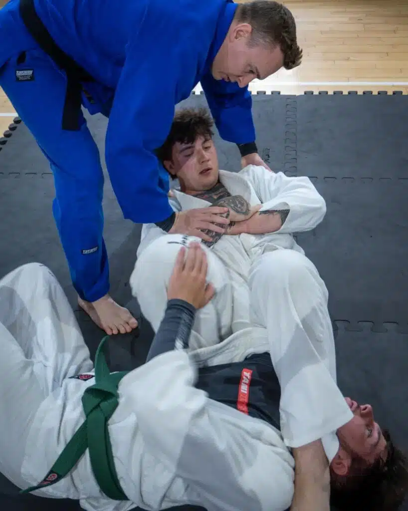 Instructor in a blue gi coaching two students during a groundwork drill