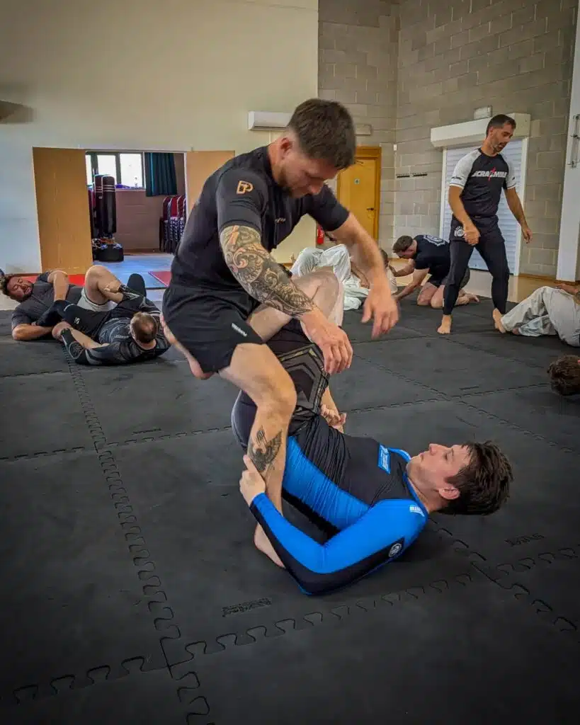 Two no-gi grapplers rolling while others train in the background