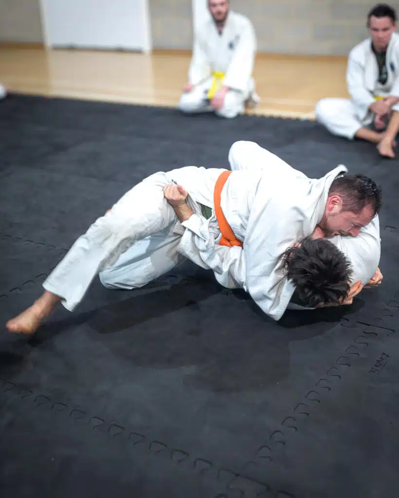Two students grappling on the mat, one securing a head and arm control