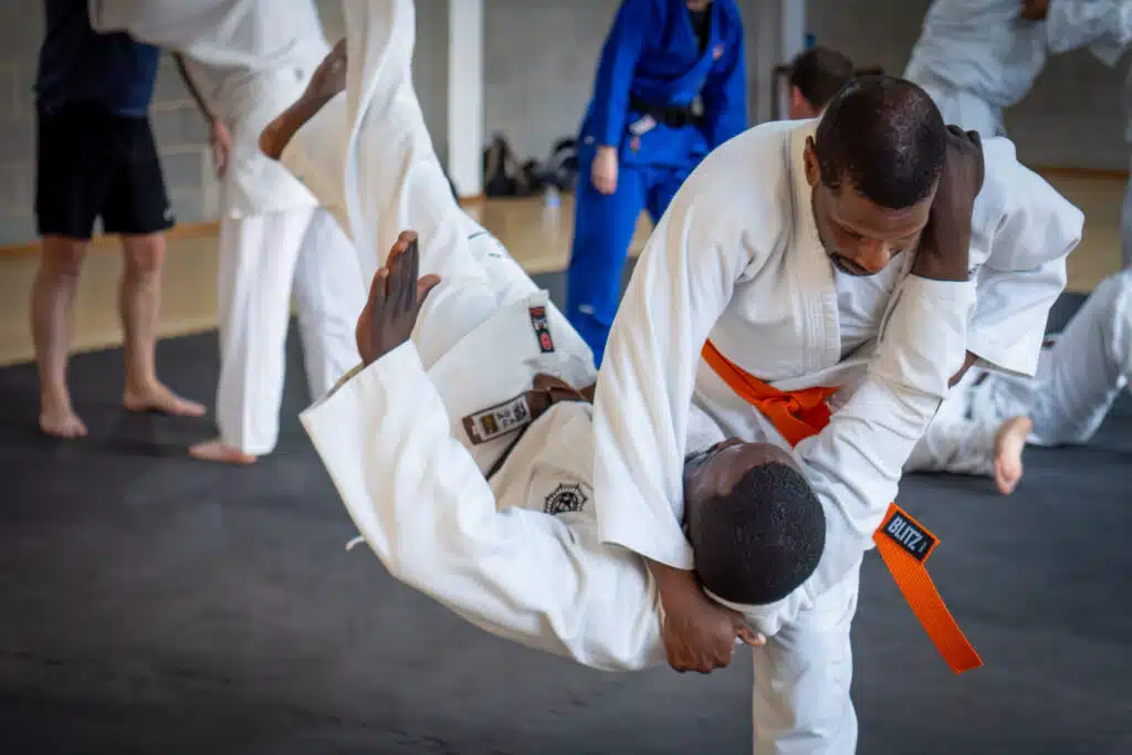 Jujutsu student being thrown over a partner's hip by an orange belt