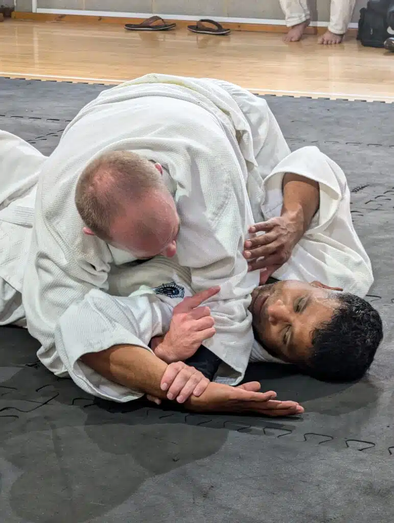 Student in a gi pinning his partner with an arm lock on the mat